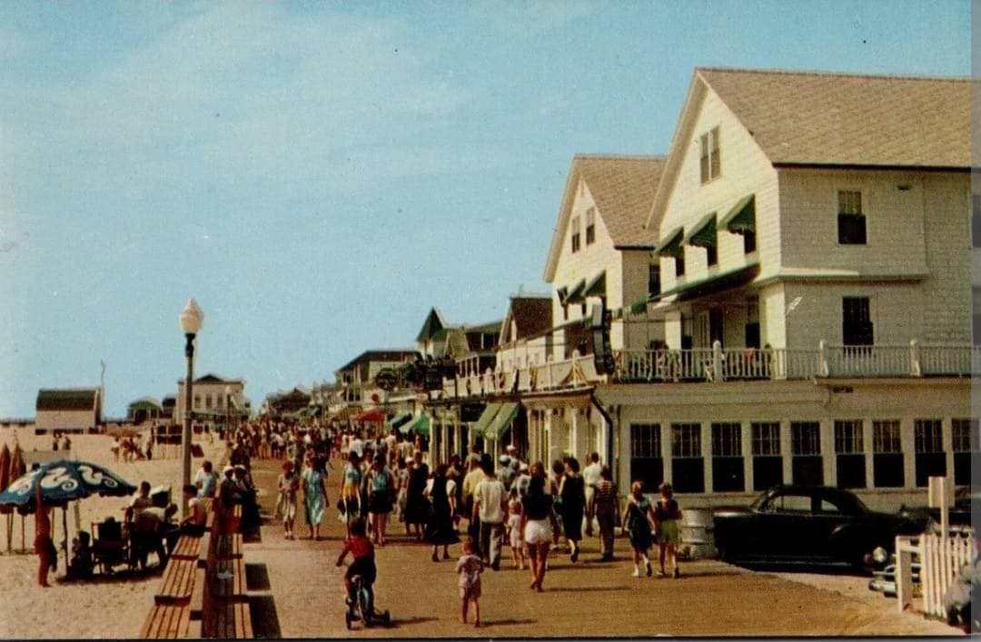 Mid-century postcard view south along the Boardwalk with hotels and parked cars.